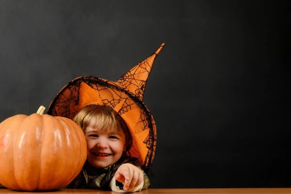 Bambino sorridente con cappello da strega accanto a una zucca.