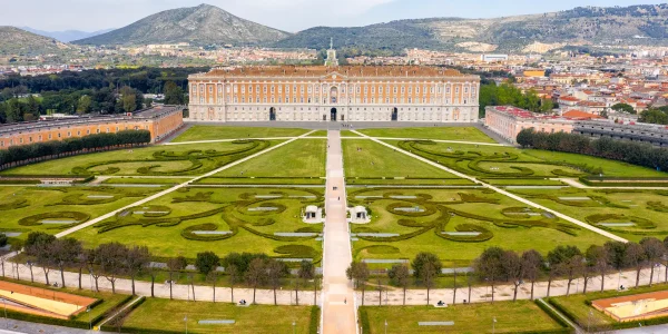 Veduta aerea della Reggia di Caserta con i suoi giardini curati sullo sfondo.