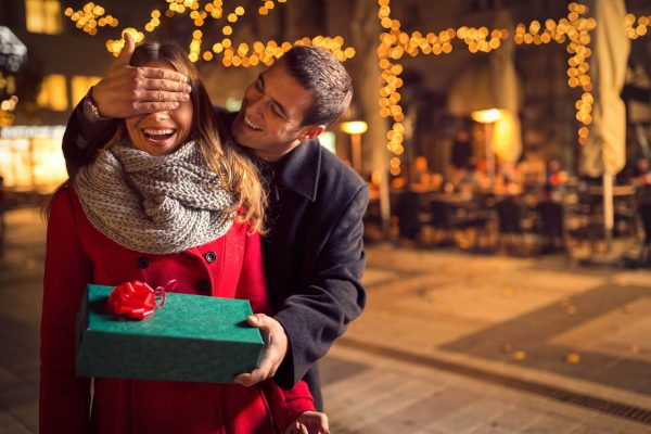 Un uomo regala una sorpresa con un pacco regalo a una donna in una strada illuminata.